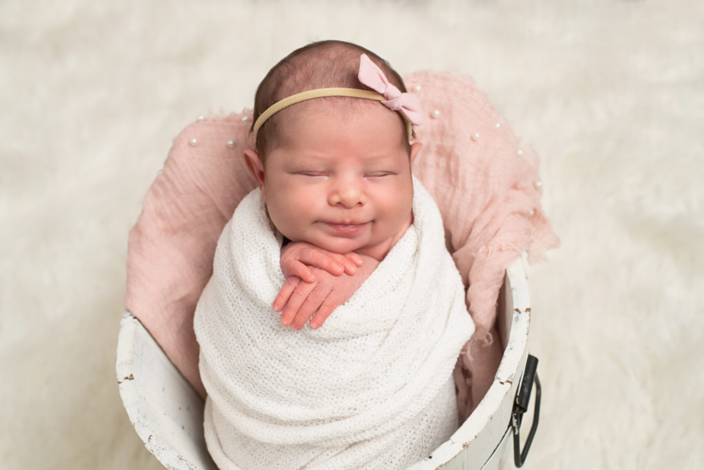 Smiling newborn wrapped up in bucket.