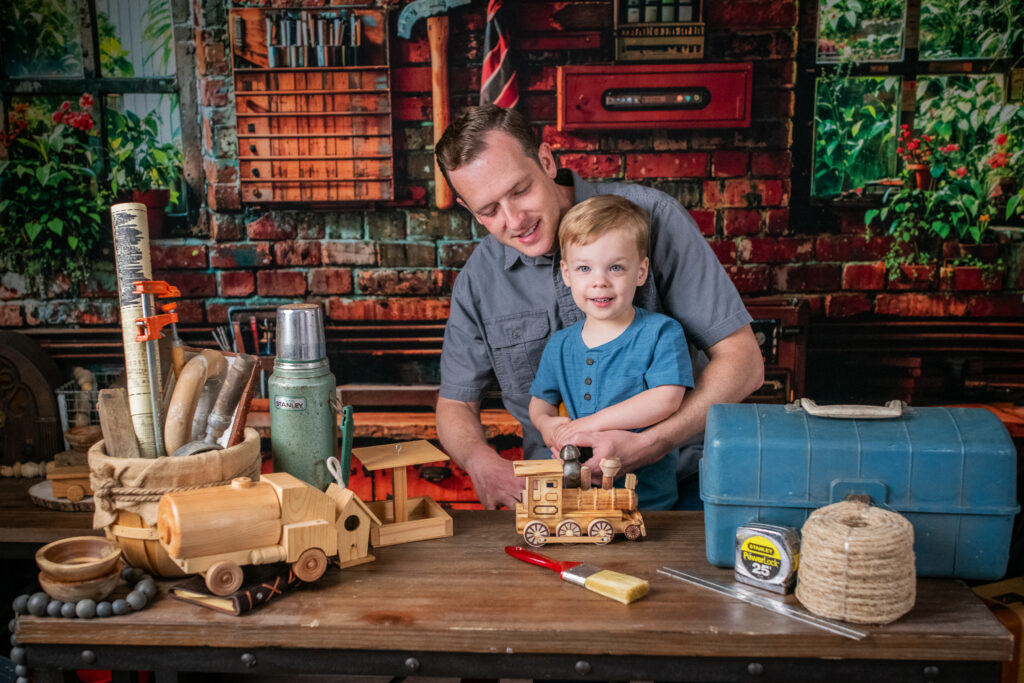 Father helping son with wooden train in workshop