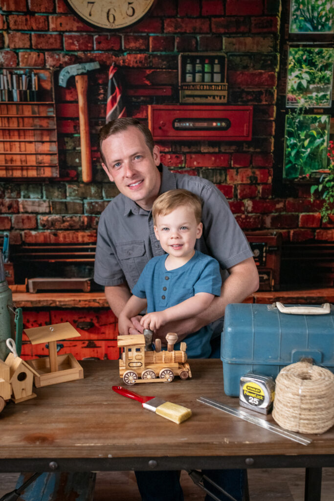 Happy Father helping son with wooden train in workshop